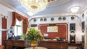 Een luxueuze hotel lobby met een weelderige kroonluchter, een receptiebalie en versierde wanddecoraties.