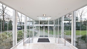 A modern glass elevator entrance with a clear view of the outdoors. - Select Hotel Silence Garden (Cologne)