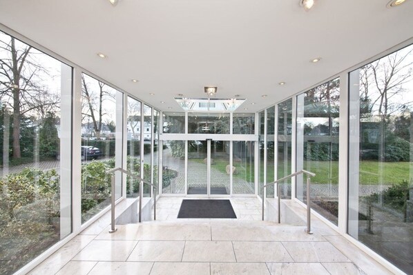 A modern glass elevator entrance with a clear view of the outdoors. - Select Hotel Silence Garden (Cologne)