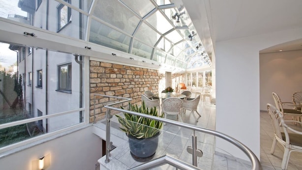 A modern interior with a glass ceiling, stone wall, and a dining area with chairs and a table. - Select Hotel Silence Garden (Cologne)