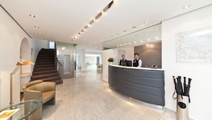A modern hotel lobby with a reception desk, a staircase, and a seating area. - Select Hotel Silence Garden (Cologne)