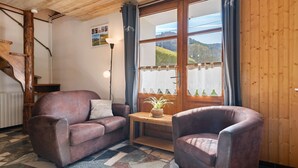 Une pièce avec un plafond en bois, un escalier, un canapé en cuir marron, une table en bois ornée d’une plante, et une grande fenêtre donnant sur une montagne.