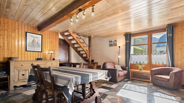 Un intérieur en bois comprenant une table à manger, des chaises, un escalier et une vue dégagée sur l’extérieur grâce à de grandes fenêtres.