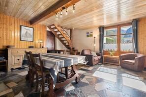 Een houten interieur met een eettafel, stoelen, een trap en uitzicht door grote ramen.