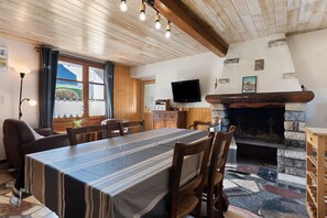 Un comedor con una mesa larga, sillas de madera, una chimenea y un televisor montado en la pared.