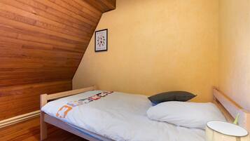 Una cama individual con colchón blanco y almohada, cabecera de madera, un cuadro enmarcado en la pared y una lámpara de noche.