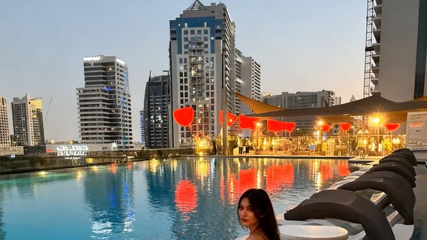 A woman sitting on a floating lounge chair in a pool with a cityscape in the background. - Vogue| Downtown close to Burj Khalifa | Dubai Mall (Dubai)