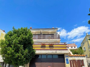 Ein mehrgeschossiges Gebäude mit einer Garage, umgeben von Grünflächen, unter blauem Himmel.