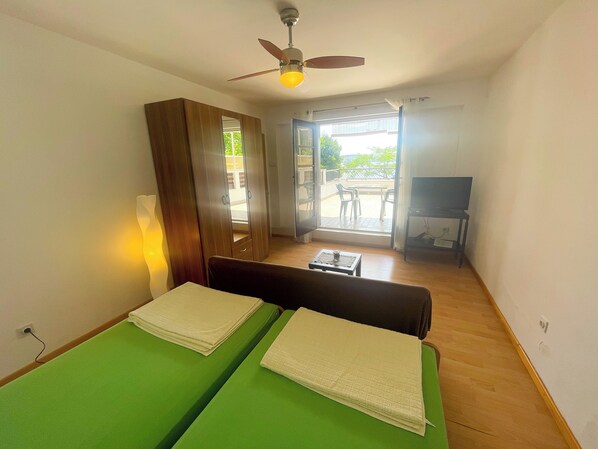 Une chambre avec deux lits, un ventilateur de plafond, une télévision et une vue sur le balcon extérieur.