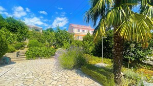 Ein gepflasterter Weg führt zu einem Gebäude mit rotem Dach, umgeben von üppiger Vegetation und einer Palme.
