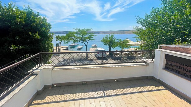 Eine Terrasse mit Meerblick, Sitzgelegenheiten im Freien und einem Geländer.