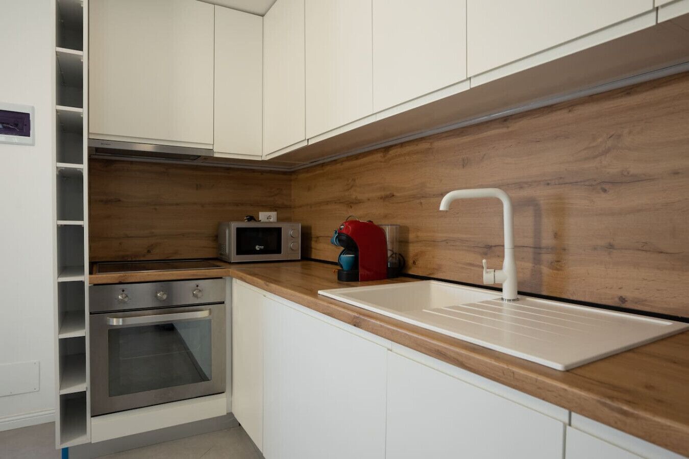 Une cuisine moderne avec des armoires blanches, un plan de travail en bois, un four encastré, un four à micro-ondes et un évier avec un robinet.