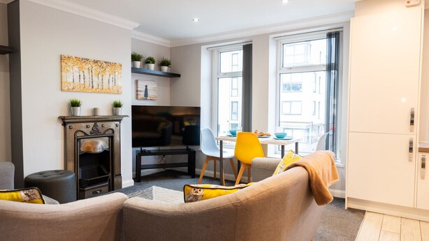 Een moderne woonkamer met een open haard, een eethoek met een tafel en stoelen, en grote ramen die zorgen voor natuurlijk licht.