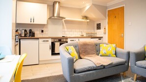 Een kleine keuken met witte kastjes, een roestvrijstalen afzuigkap en een houten deur.