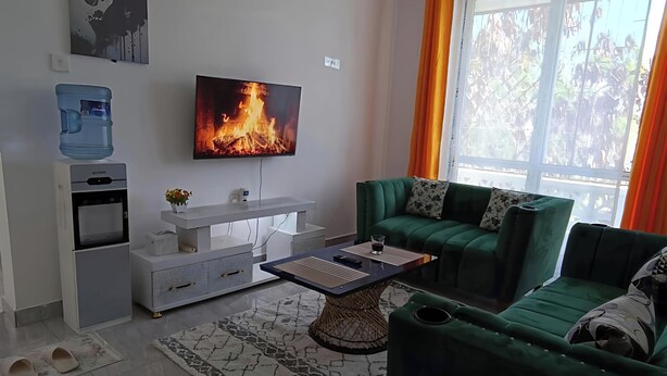 A modern living room with a flat-screen TV, a water dispenser, a mini-fridge, a sofa, and a coffee table. - Greyline luxe Bamburi. O743 for 379 then I35. (Mombasa)