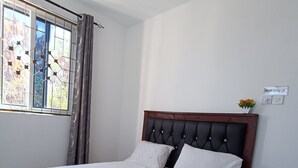 A neatly made bed with white linens, a wooden headboard, and a small bedside table with a vase of flowers. - Greyline luxe Bamburi. O743 for 379 then I35. (Mombasa)
