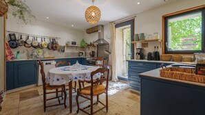 A kitchen with a dining table, chairs, hanging pots, and a window with a view. - Guest Room “L’Aphyllanthe” with Large Shared Courtyard and Wi-Fi (Saint-Remèze)