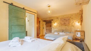 A room with two beds, a green sliding door, a stone wall, and a hanging map. - Guest Room “L’Aphyllanthe” with Large Shared Courtyard and Wi-Fi (Saint-Remèze)
