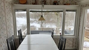 Ein Essbereich mit großem Tisch und Stühlen, großen Fenstern mit Blick auf eine verschneite Landschaft und einer hängenden Leuchte.