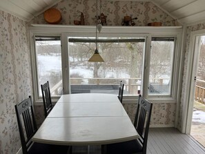 A dining area with a large table and chairs, large windows with a view of a snowy landscape, and a hanging light fixture. - 4 Person Holiday Home in Ingaro (Värmdö)
