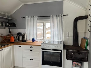A kitchen with white cabinets, a stove, a coffee maker, and a window with curtains. - 4 Person Holiday Home in Ingaro (Värmdö)