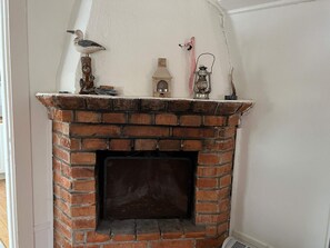A brick fireplace with a metal grate, a small bird figurine, and a lantern on top. - 4 Person Holiday Home in Ingaro (Värmdö)