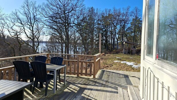Eine Holzterrasse mit Tisch und Stühlen, mit Blick auf einen See und Bäume.