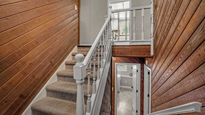 Un escalier en bois avec des balustrades blanches, des marches recouvertes de moquette et une vue sur une pièce dotée d’une porte et d’une fenêtre.
