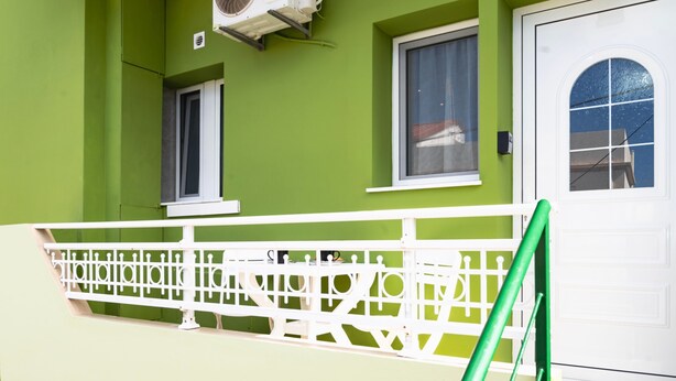 Un edificio con fachada verde, ventanas blancas y una puerta blanca con panel de vidrio.