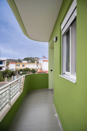 Ein Balkon mit grüner Wand, weißem Fensterrahmen und Fliesenboden.