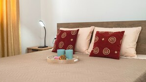 Una cama bien hecha con almohadas estampadas, una mesita de noche con lámpara y una bandeja con donas.