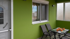 Una habitación con paredes verdes, una puerta blanca, una ventana con persiana blanca y una mesa con sillas y alimentos para el desayuno.