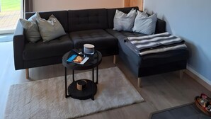 A modern living room with a sectional sofa, a round wall clock, and a view of the outdoors. - Holiday Home Apfelblüte in Swedish Style on Pellworm (Pellworm)