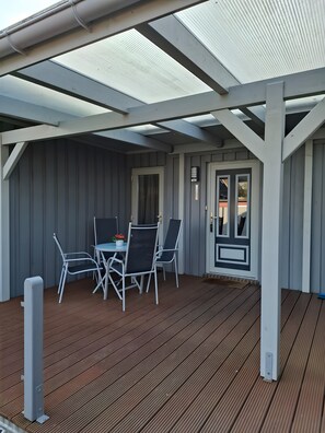 Un espace extérieur abrité, avec une table et des chaises, une porte et une vue sur le ciel à travers la structure du toit.