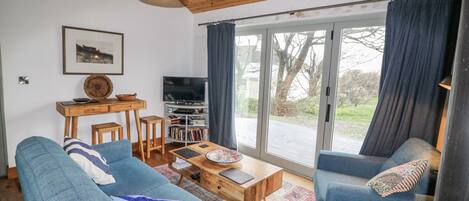 A modern living room with two blue sofas, a wooden coffee table, a TV on a stand, and a large window with curtains.