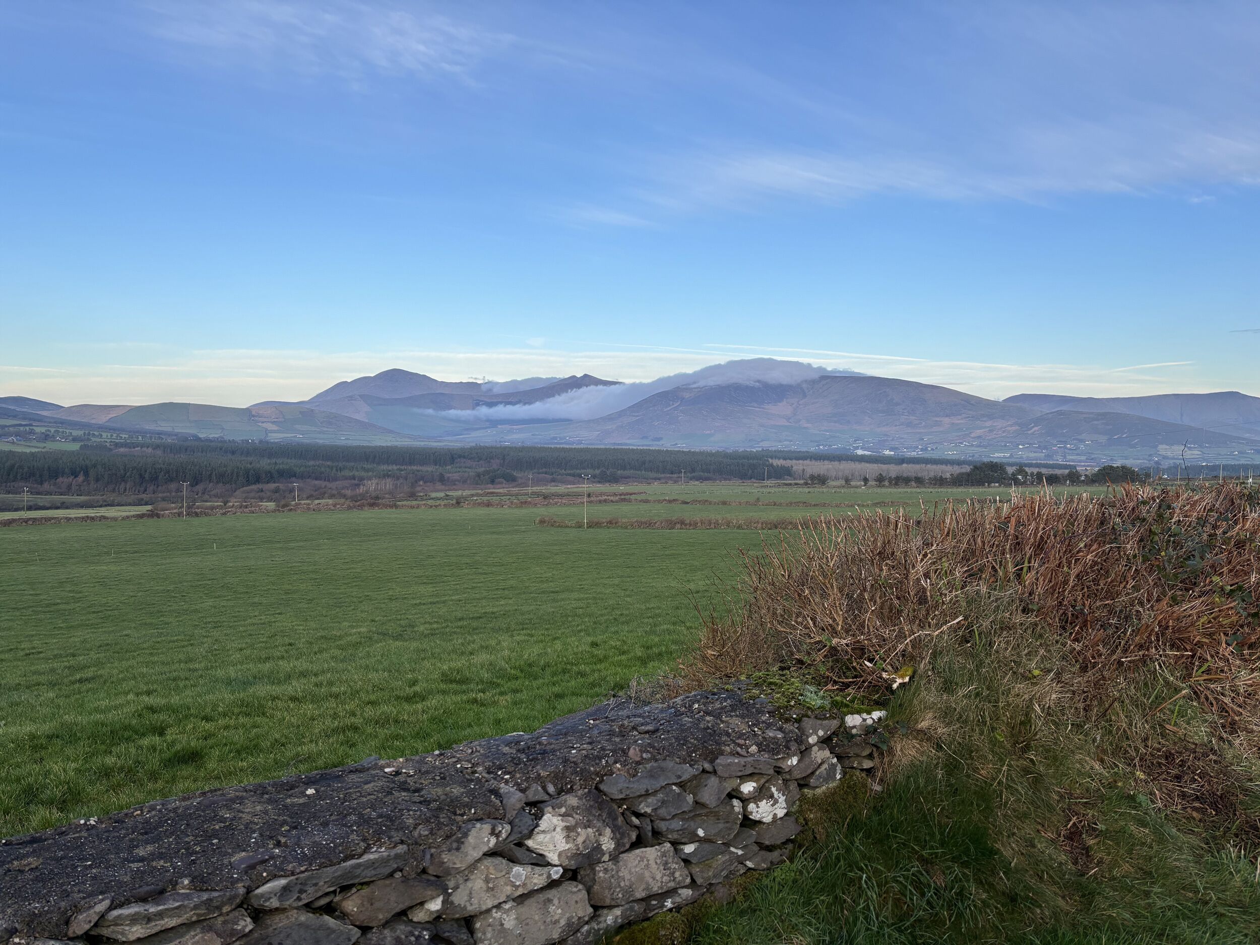 A stone wall with a grassy field and distant mountains.