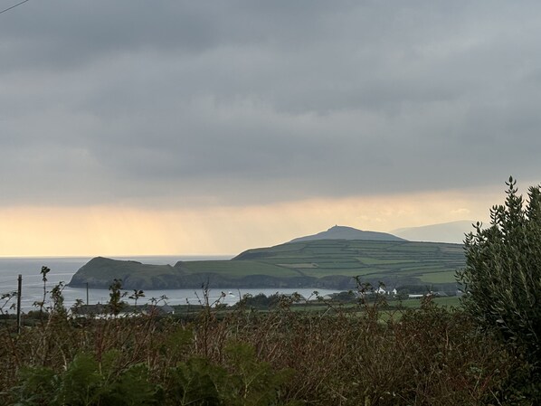 A coastal landscape with rolling hills, a body of water, and a cloudy sky. - Bosca Neadu (Dingle)