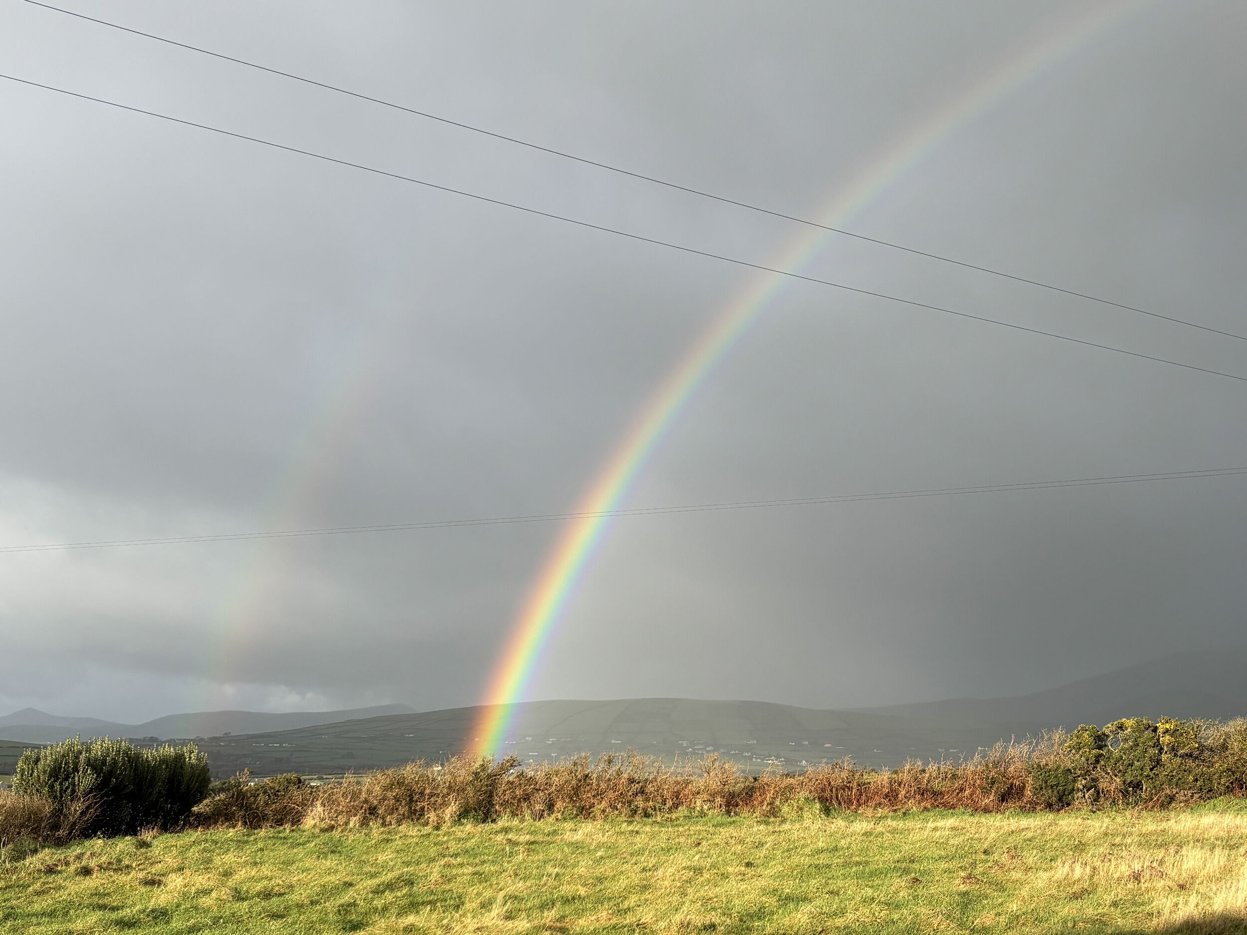 A landscape with a rainbow, power lines, and distant hills.
