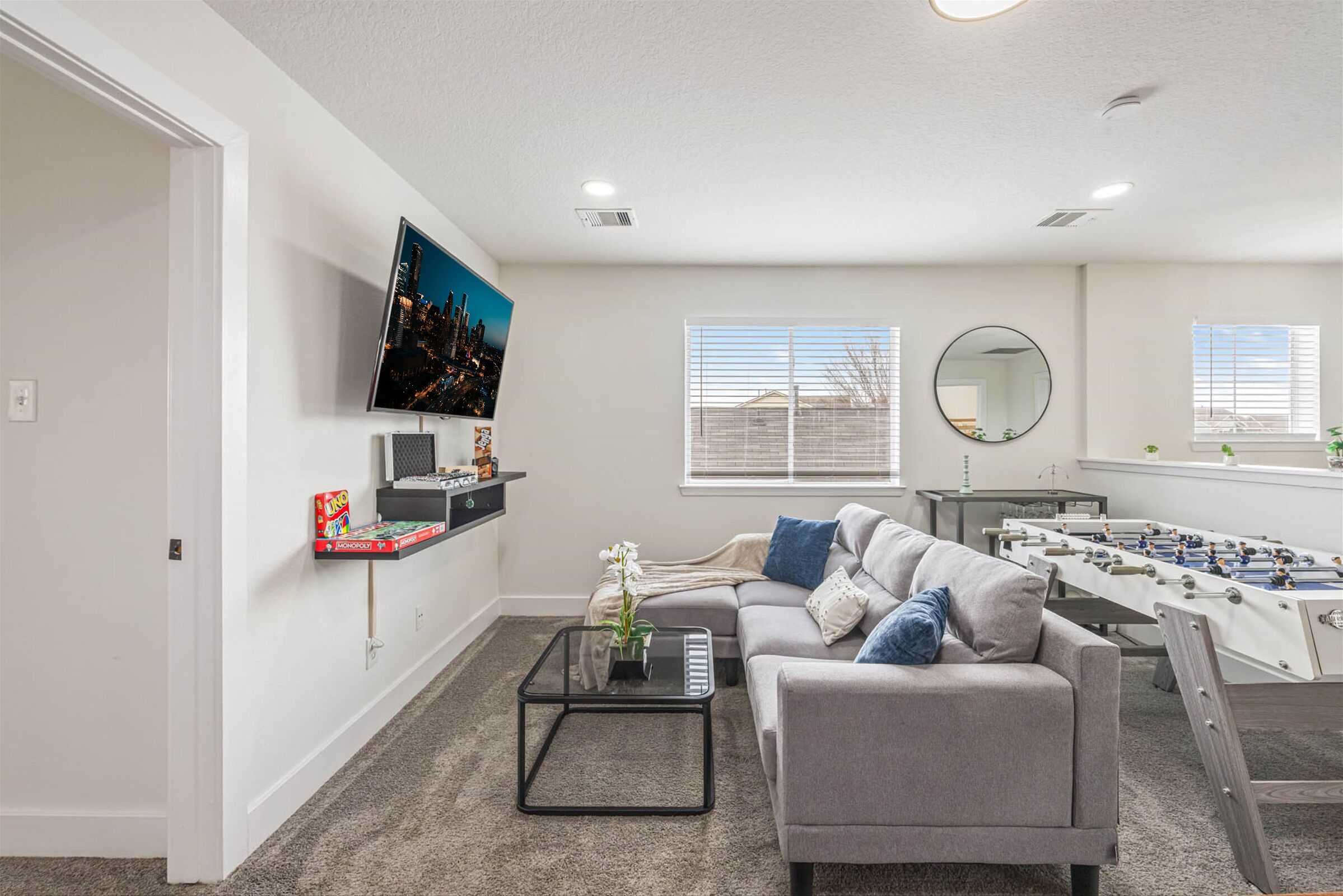 A living room with a sofa, coffee table, television, and foosball table.