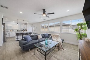 A modern living room with a sectional sofa, a glass coffee table, and a ceiling fan. - Htown Getaway | Game Room BBQ Fire Pit Sleeps 16 (Houston)