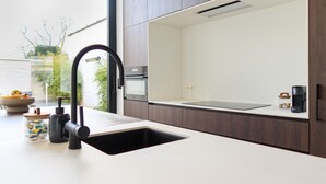 A modern kitchen with a black faucet, a white countertop, and a view of greenery outside. - Cosy Courtyard House Hasselt (Hasselt)