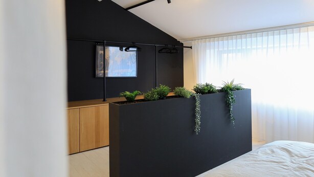 A modern bedroom with a black accent wall, a bed, a wooden cabinet, and a window with sheer curtains. - Cosy Courtyard House Hasselt (Hasselt)