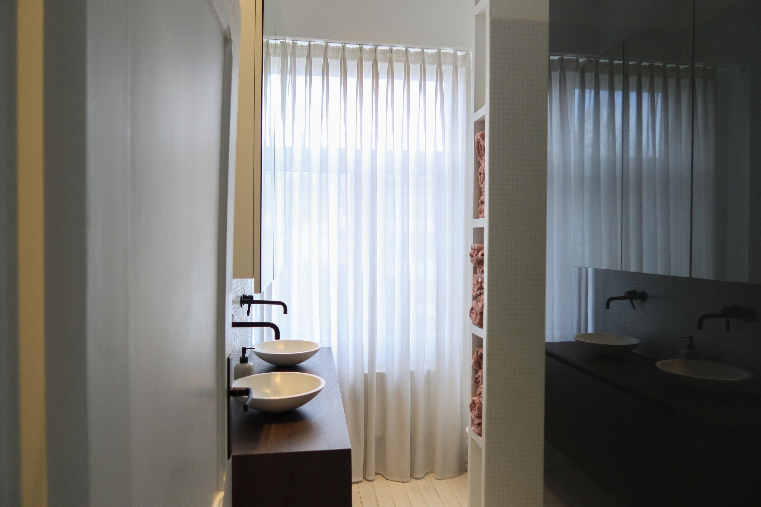 Ein Badezimmer mit zwei Waschbecken, einem Spiegel und einem Fenster mit Vorhängen.
