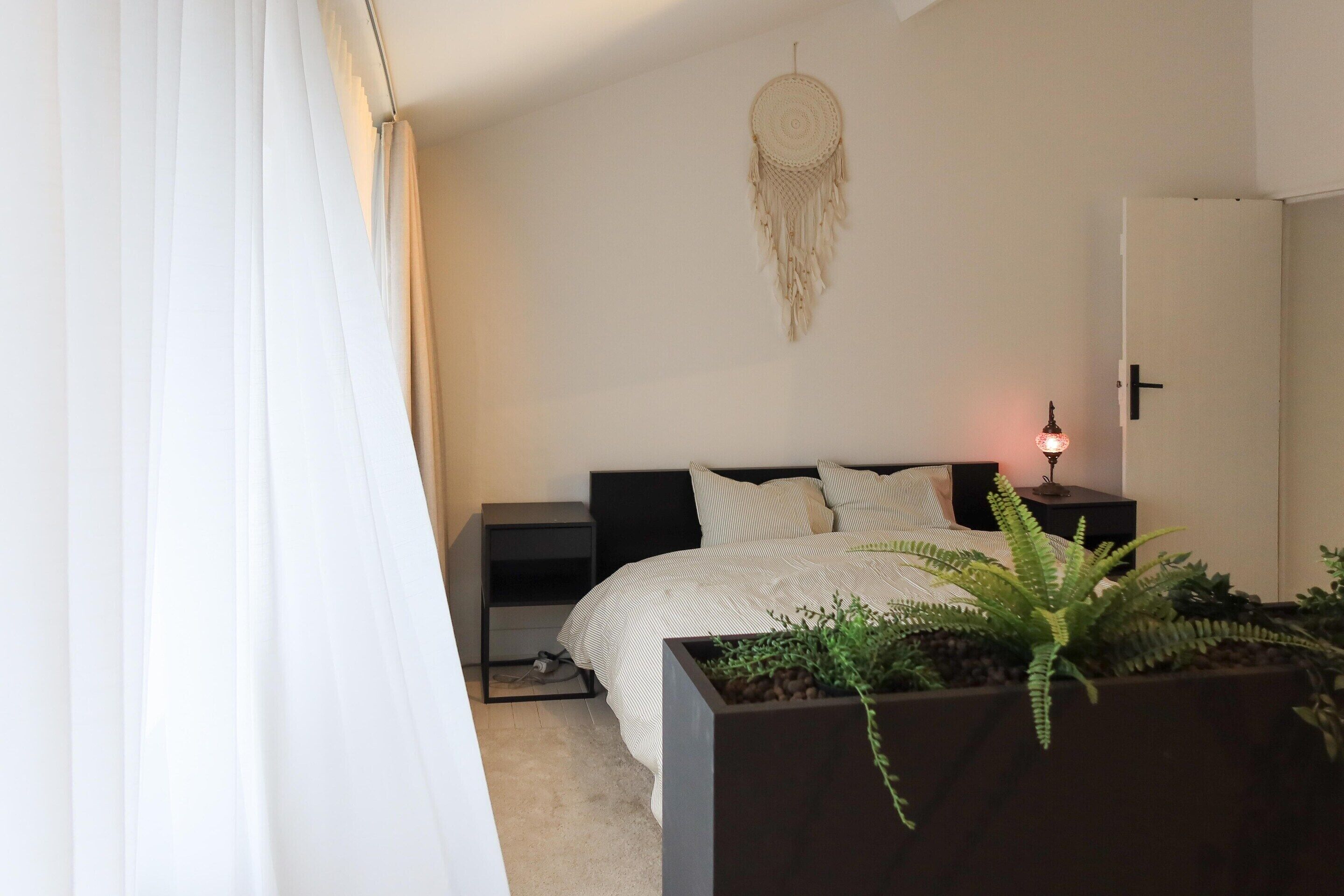 Ein Schlafzimmer mit Bett, Nachttischen, einer Ablagefläche, einem Traumfänger und einer Topfpflanze.