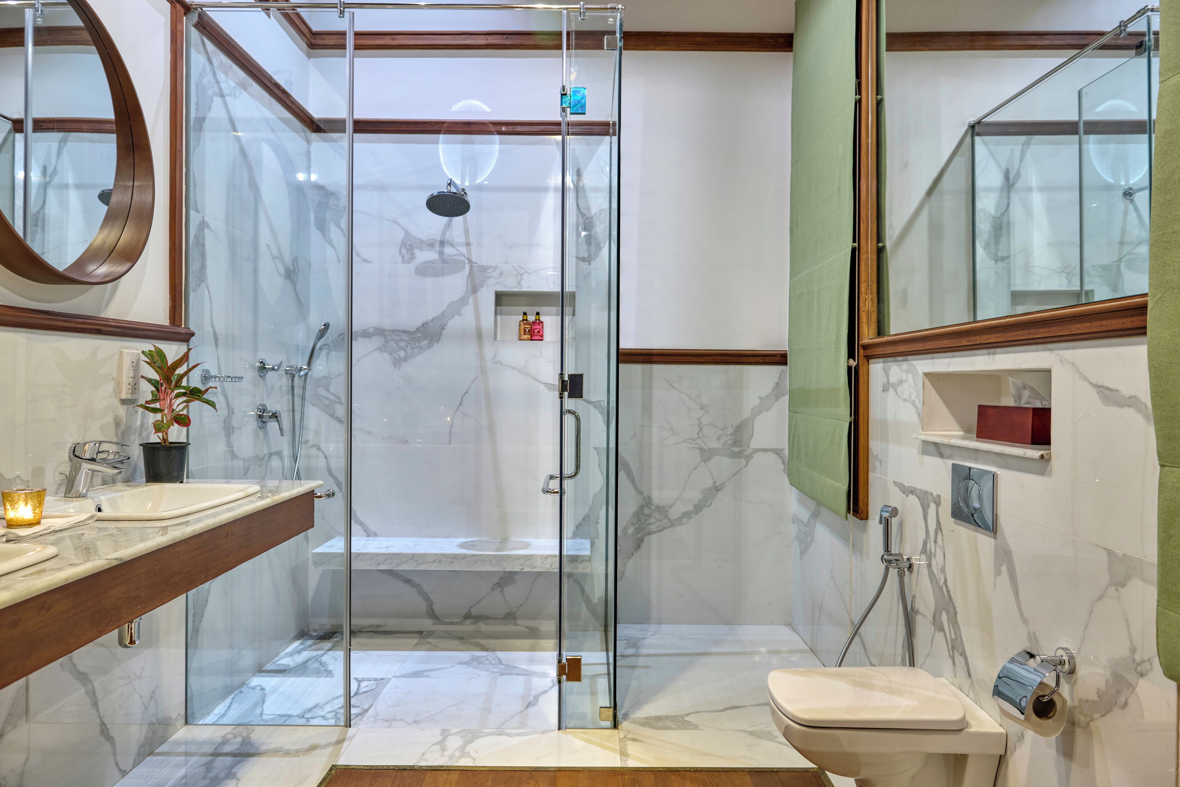 A modern bathroom with a glass-enclosed shower, a marble-tiled floor, a wooden vanity, and a toilet.