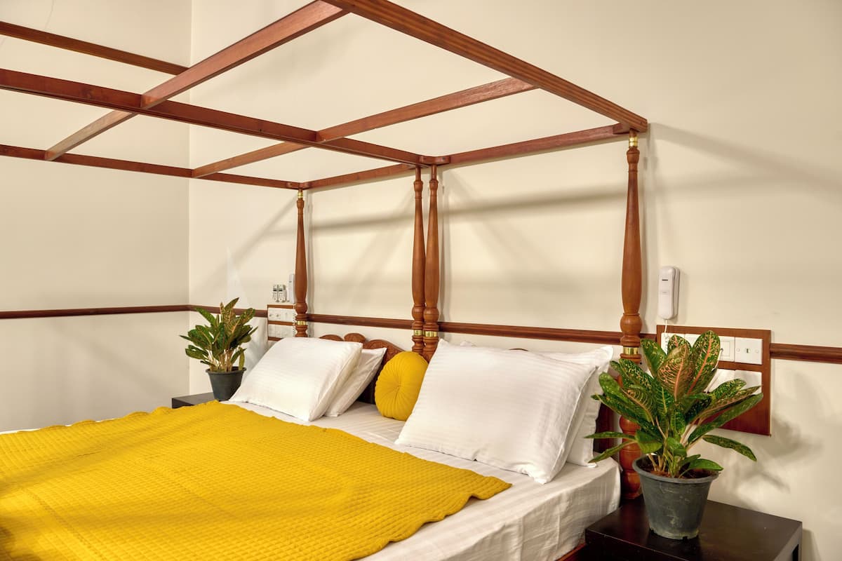 A bed with a wooden headboard, white bedding, and a yellow throw blanket. There are two potted plants on the nightstand.