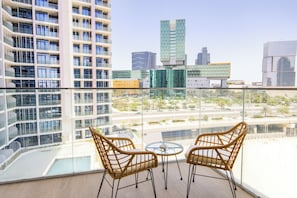 Un balcon avec deux fauteuils en osier et une petite table, d’où l’on peut admirer un paysage urbain avec des bâtiments modernes.