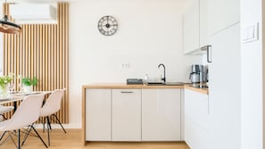 Una cucina moderna con un piano di lavoro in legno, mobili bianchi, una sveglia nera e un'area pranzo con sedie e tavolo.