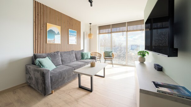 Un salon moderne avec un canapé, une table basse et une vue sur la ville grâce à de grandes fenêtres.