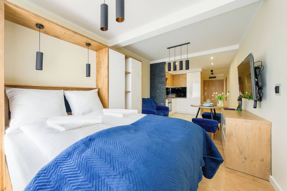 Un dormitorio moderno con una cama grande, un cabecero de madera, una manta azul y un escritorio con una silla.